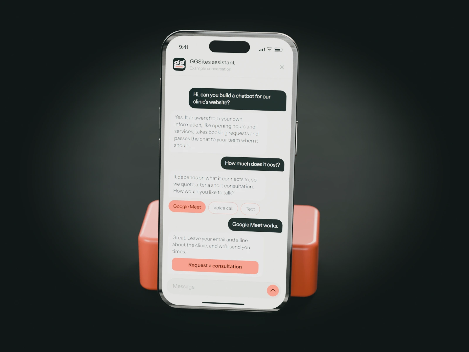 A phone on a coral stand showing a website chat: a visitor asks for a chatbot for their clinic and the assistant offers a consultation.