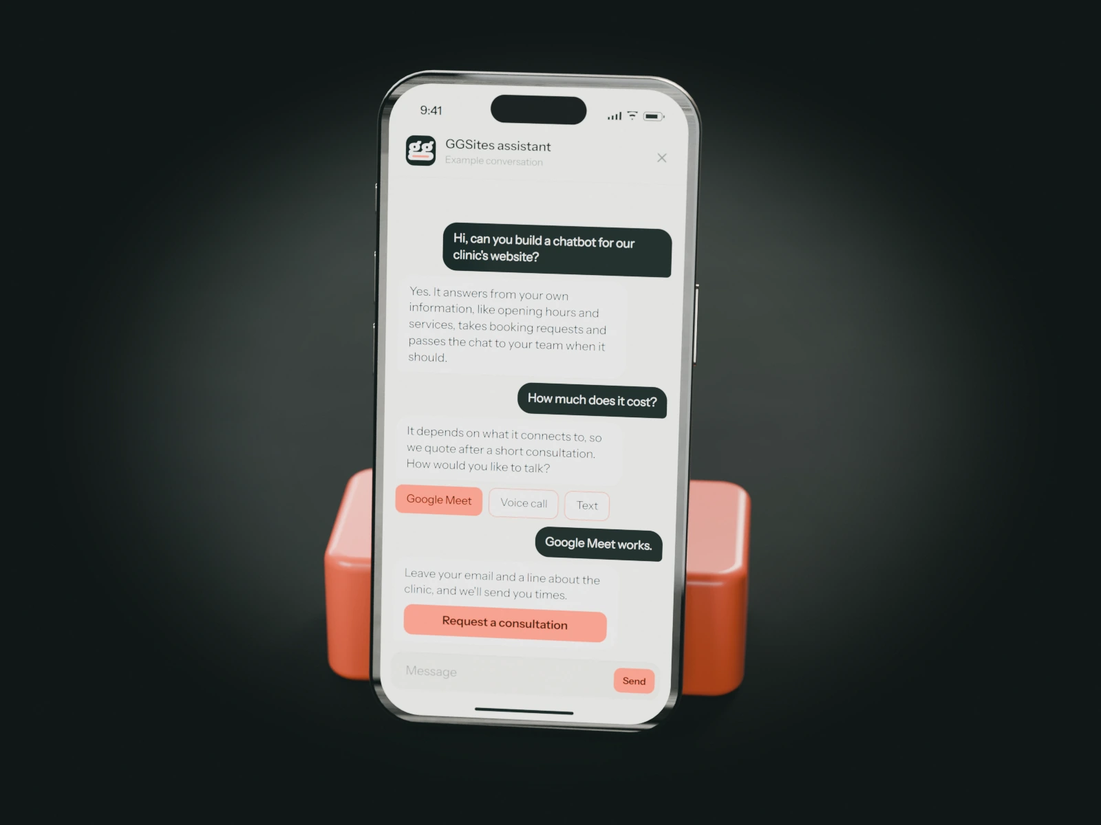 A phone on a coral stand showing a website chat: a visitor asks for a chatbot for their clinic and the assistant offers a consultation.